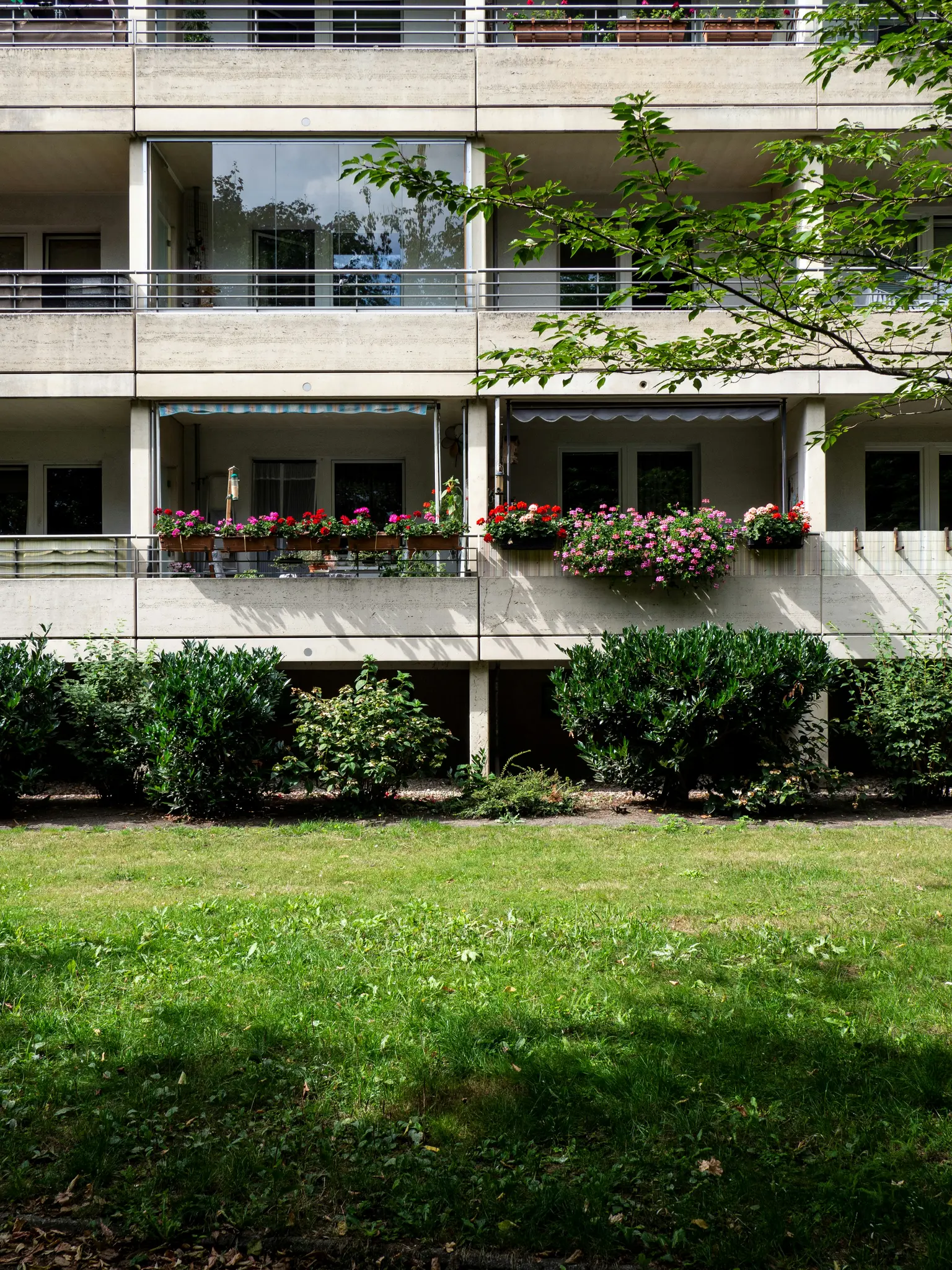 Un edificio de apartamentos de hormigón con múltiples balcones, algunos cerrados con vidrio, otros abiertos con jardineras