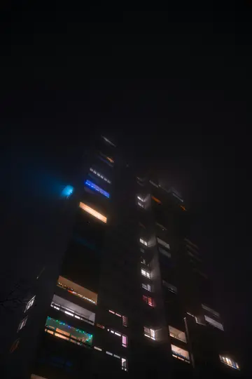 Una toma en ángulo bajo de un edificio residencial alto y oscuro por la noche. Varias ventanas y balcones brillan en blanco