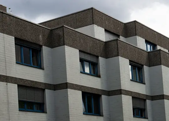 Edificio de varias plantas con fachada de ladrillo blanco y bandas horizontales de material texturizado gris oscuro.