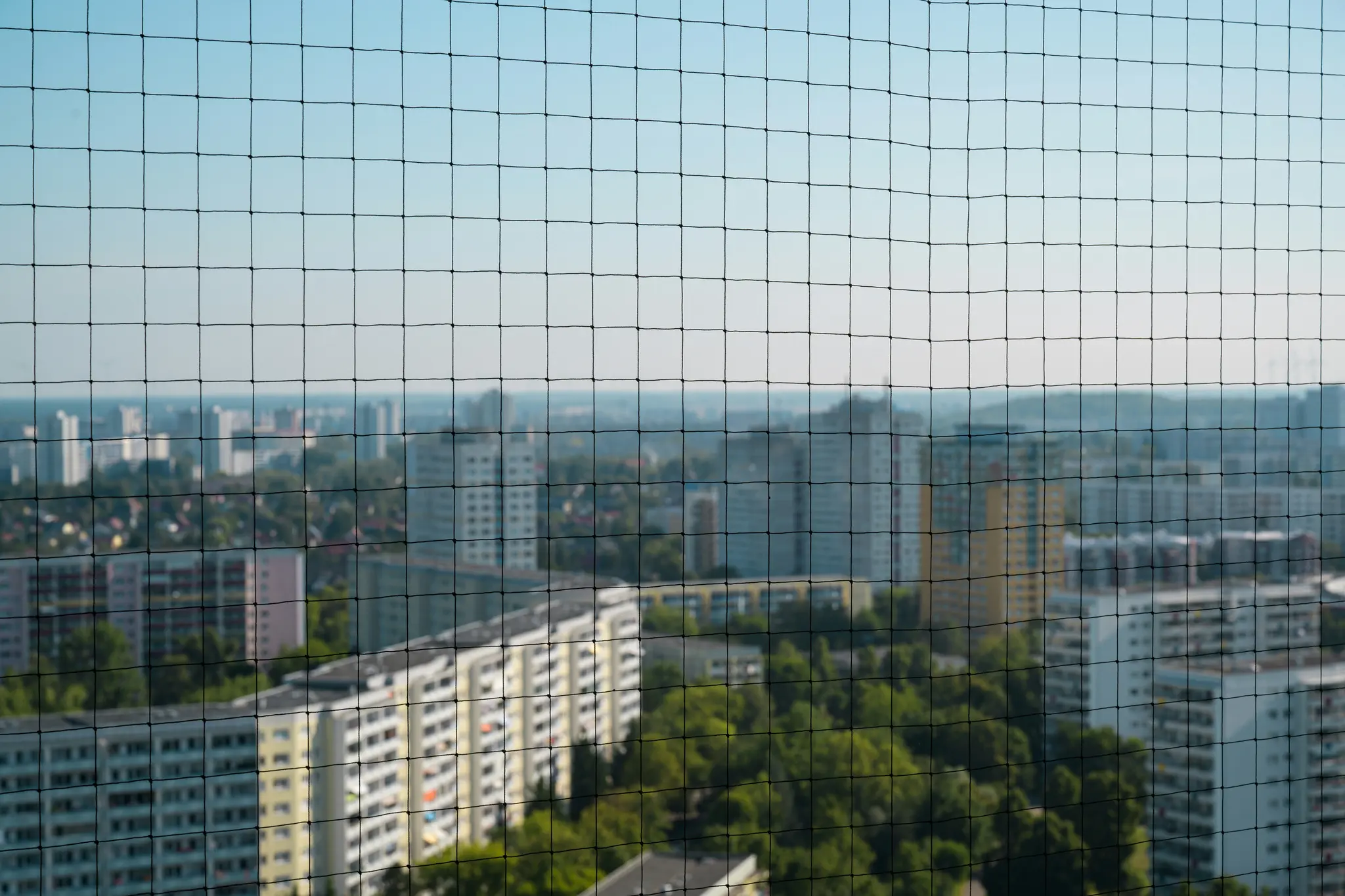 Čierna sieť vypĺňa popredie, ostro zaostrená. Za ňou rozmazaná mestská krajina s mnohými budovami a stromami.