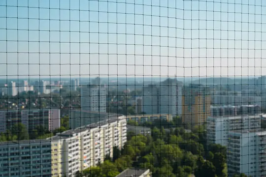 Ein schwarzes Netz füllt den Vordergrund, scharf im Fokus. Dahinter eine unscharfe Stadtlandschaft mit zahlreichen Gebäuden
