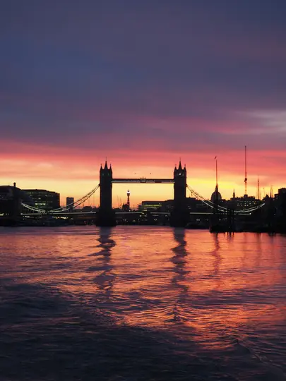 Široký záber na Tower Bridge v Londýne, v siluete proti dramatickej oblohe pri západe slnka s výraznými oranžovými, červenými