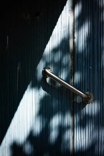 Una foto abstracta en primer plano de una puerta azul texturizada con una manija de metal plateada. La luz del sol proyecta