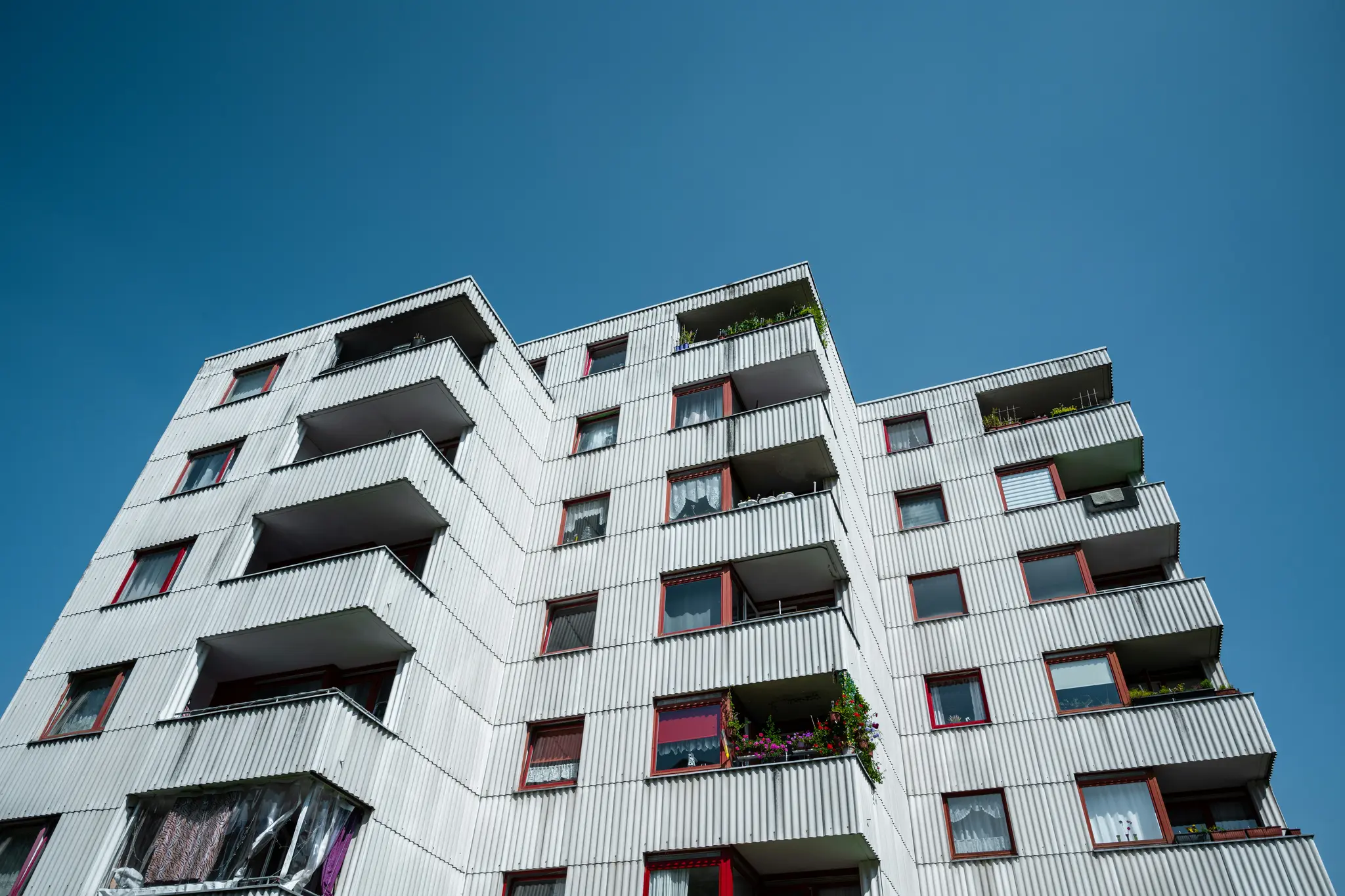 Vista desde un ángulo bajo de un edificio de apartamentos blanco de varios pisos con revestimiento corrugado, ventanas con