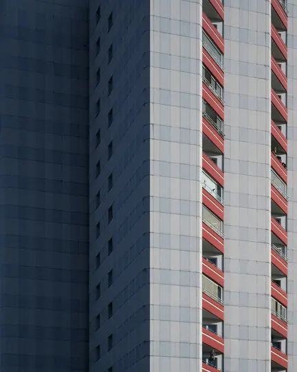 Un edificio alto con facciata piastrellata grigia e balconi rossi. Il lato sinistro è in ombra, mentre il lato destro è ben