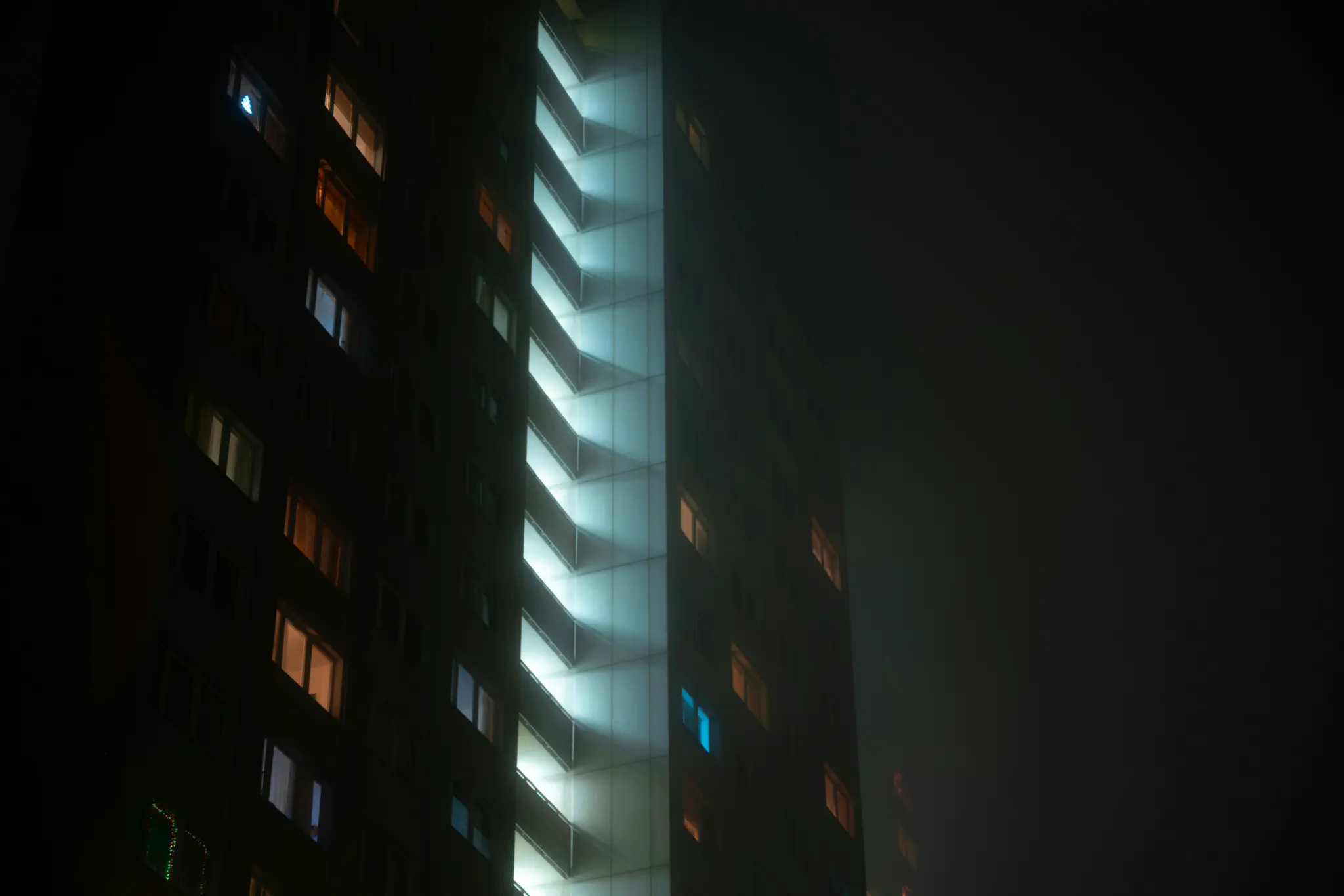 Una toma de ángulo bajo de un edificio alto por la noche, con algunas ventanas de color naranja brillante y otras azules, y