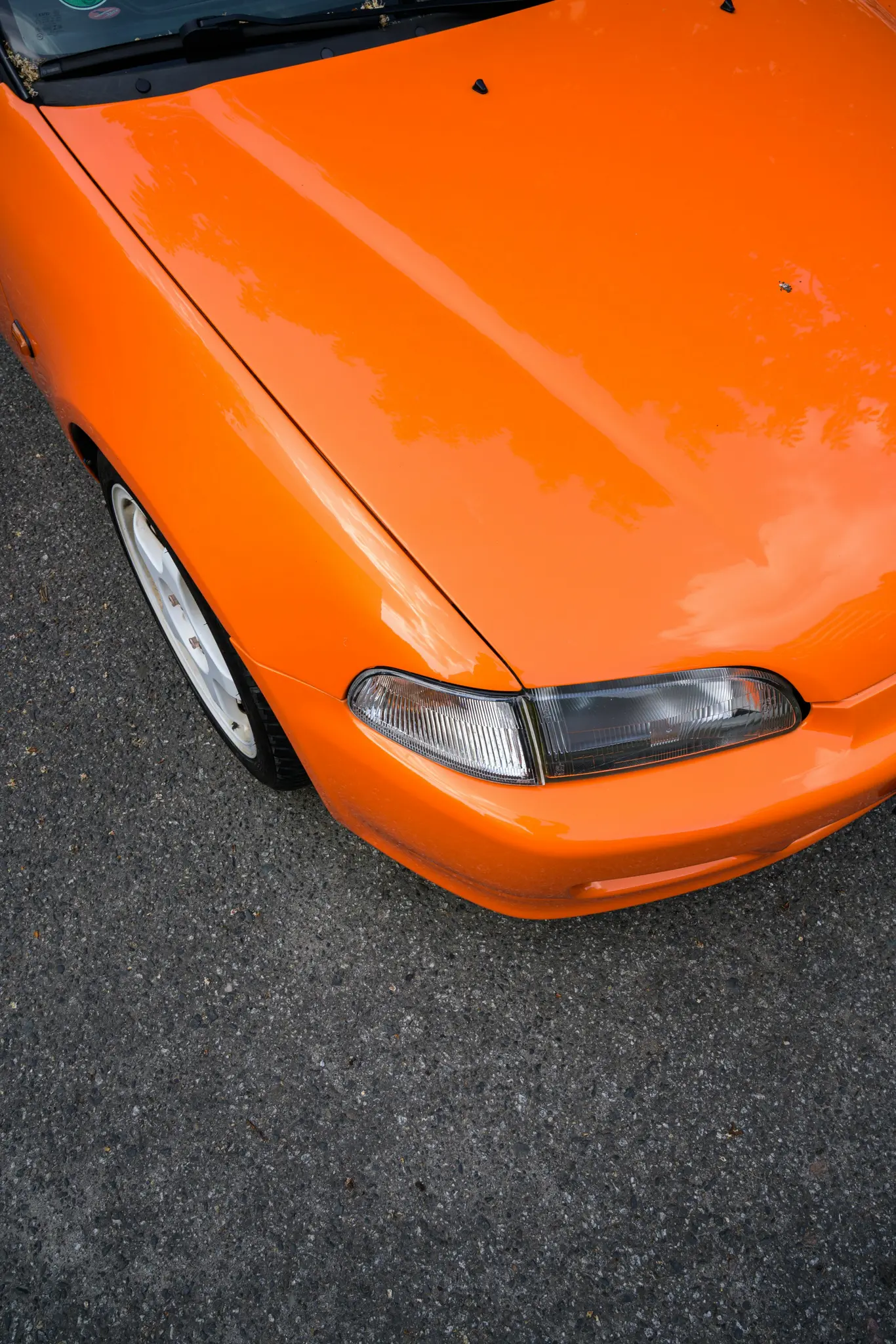 Un primer plano de ángulo alto de un coche naranja brillante y reluciente, aparcado sobre asfalto gris oscuro.
