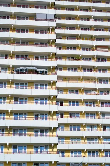 Una vista ravvicinata, a schermo intero, della facciata di un condominio a più piani con muri gialli, balconi bianchi e