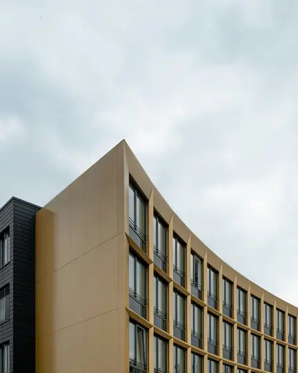 Un edificio moderno con una facciata curva, color beige dorato e sezioni grigio scuro, con molte finestre rettangolari.
