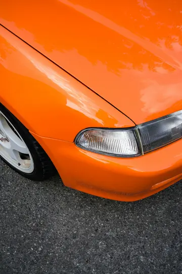 Un primer plano desde un ángulo alto del panel delantero brillante y de color naranja intenso de un coche, que muestra parte