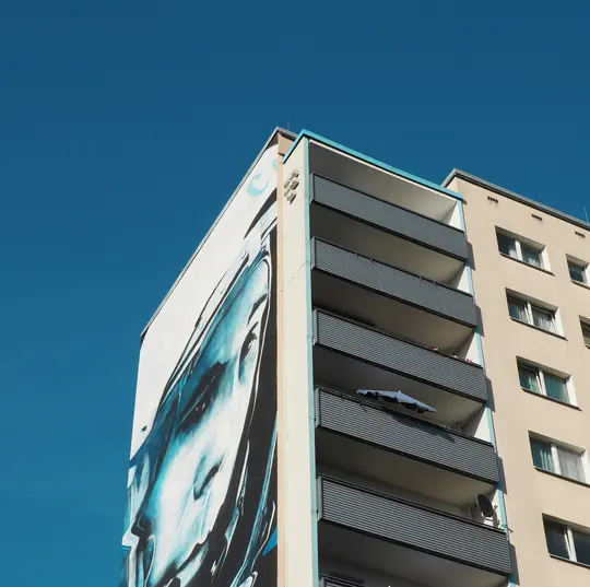 Vista da un angolo basso di un edificio alto con un grande murale blu e bianco di un volto sul lato sinistro, in contrasto