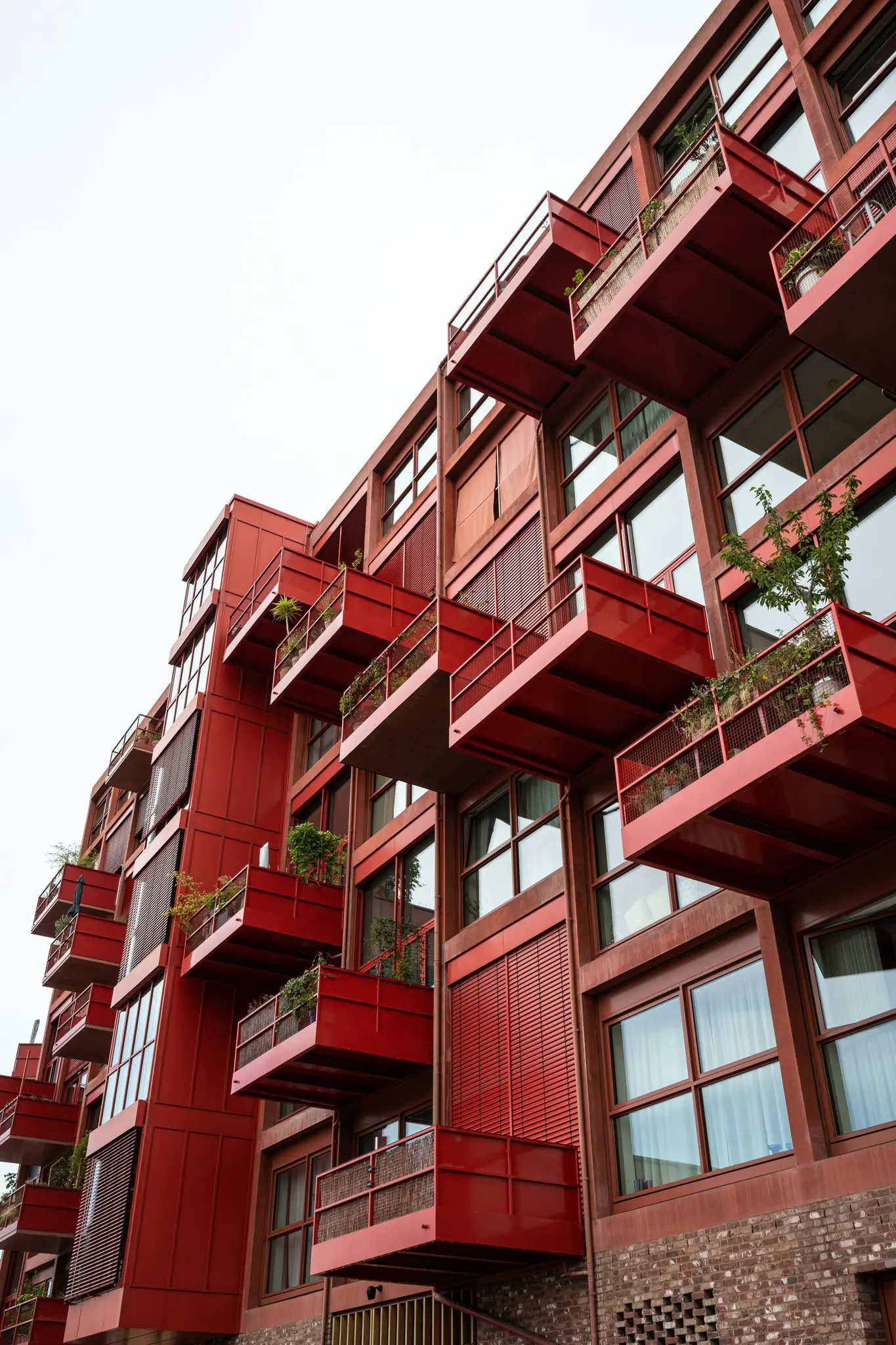Vista de ángulo bajo de un edificio moderno con numerosos balcones rojos y grandes ventanales contra un cielo brillante y