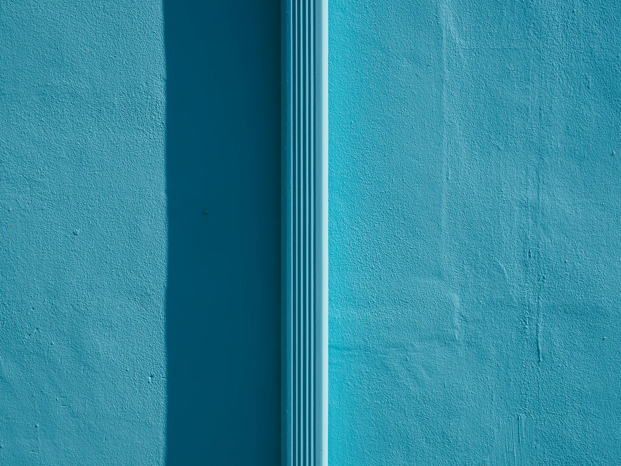 Un primer plano de una pared turquesa texturizada con una tubería acanalada vertical en el lado derecho, que proyecta una