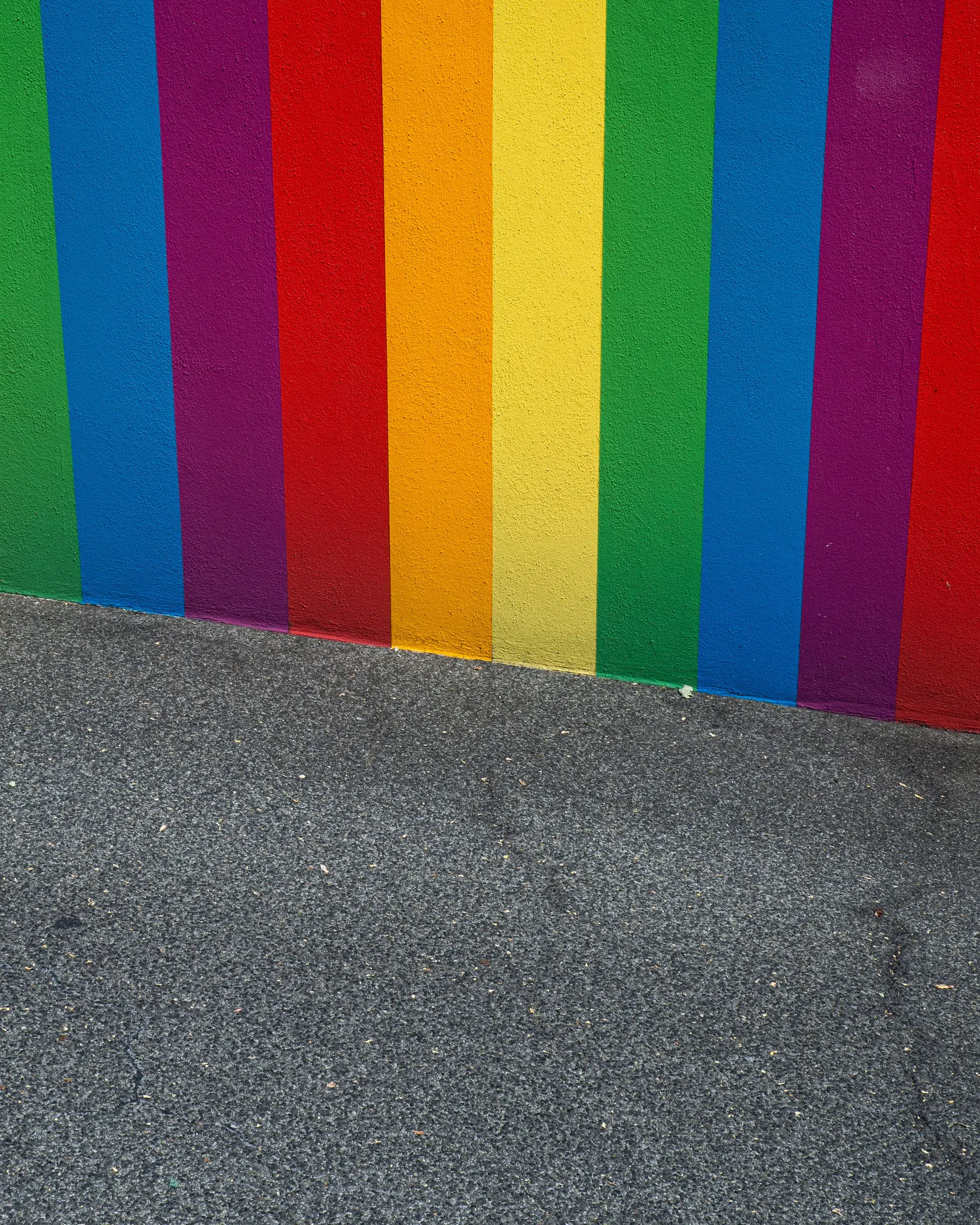Una pared vibrante pintada con rayas verticales en verde, azul, morado, rojo, naranja y amarillo, que se encuentra con un