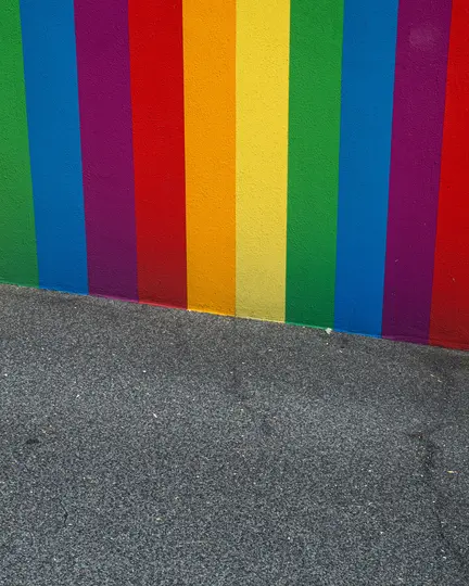 Una pared vibrante pintada con rayas verticales en verde, azul, morado, rojo, naranja y amarillo, que se encuentra con un