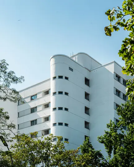 Un edificio bianco alto e moderno con una sezione curva prominente e piccole finestre rettangolari è visto dal basso