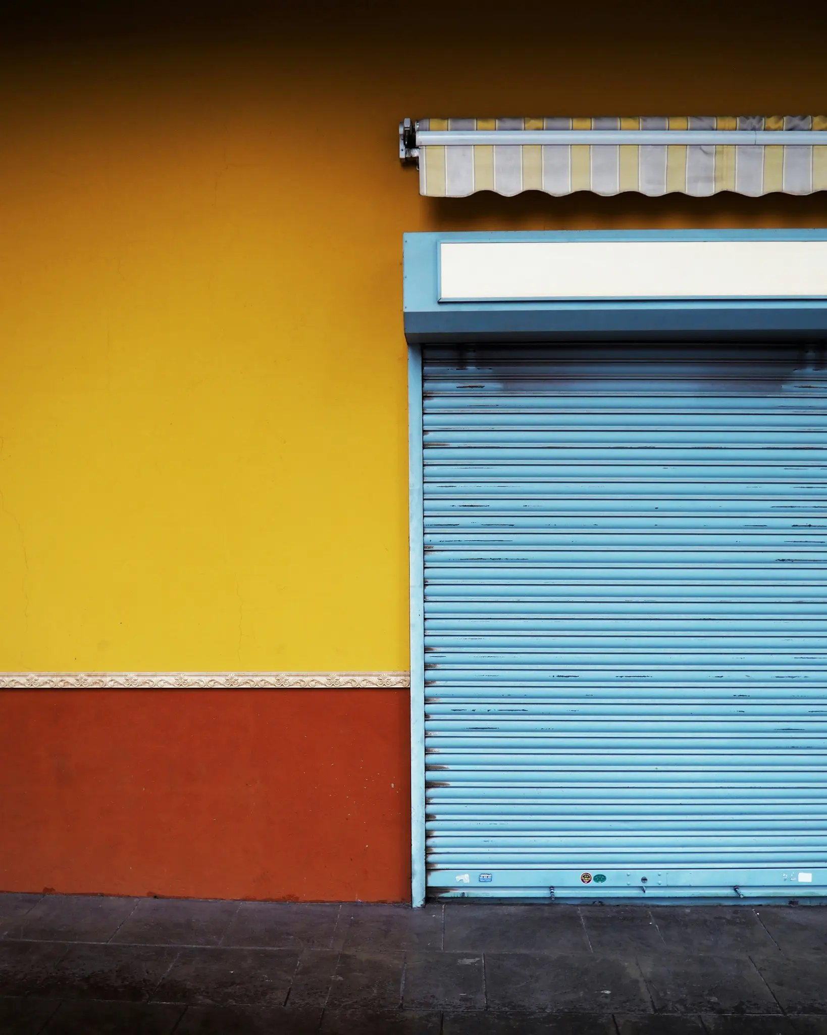 Una foto vibrante de una tienda cerrada. Una pared amarillo brillante se une a una sección inferior roja, separadas por un