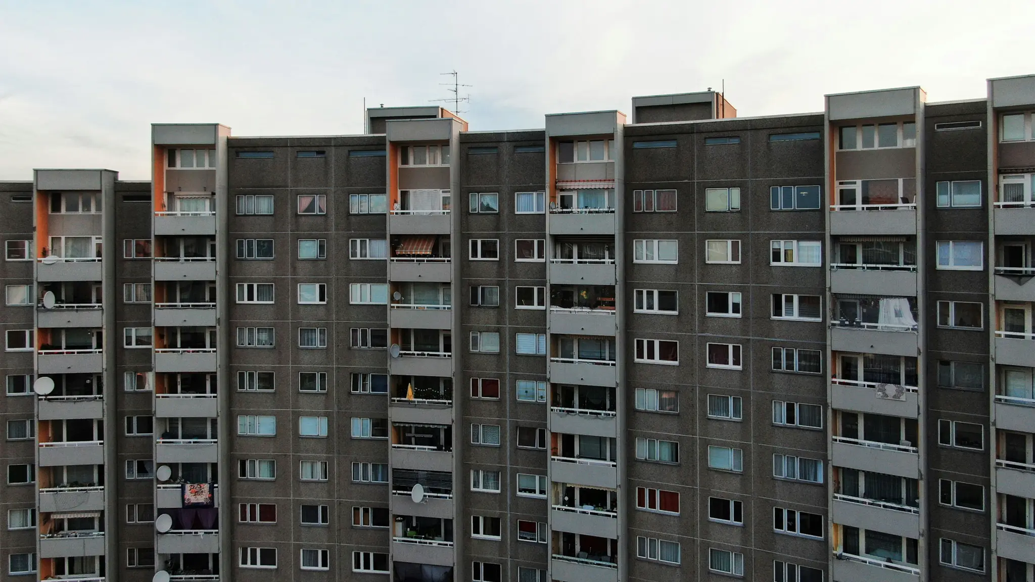 Un edificio de apartamentos de hormigón grande y gris llena el encuadre, con muchas ventanas y balcones bajo un cielo