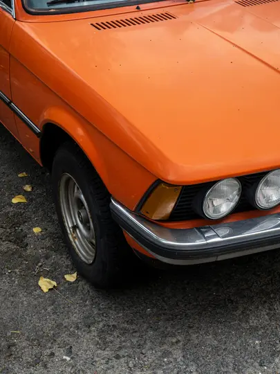 Un primo piano, scatto dall'alto del tre quarti anteriore destro di un'auto vintage arancione, che mostra il faro, il