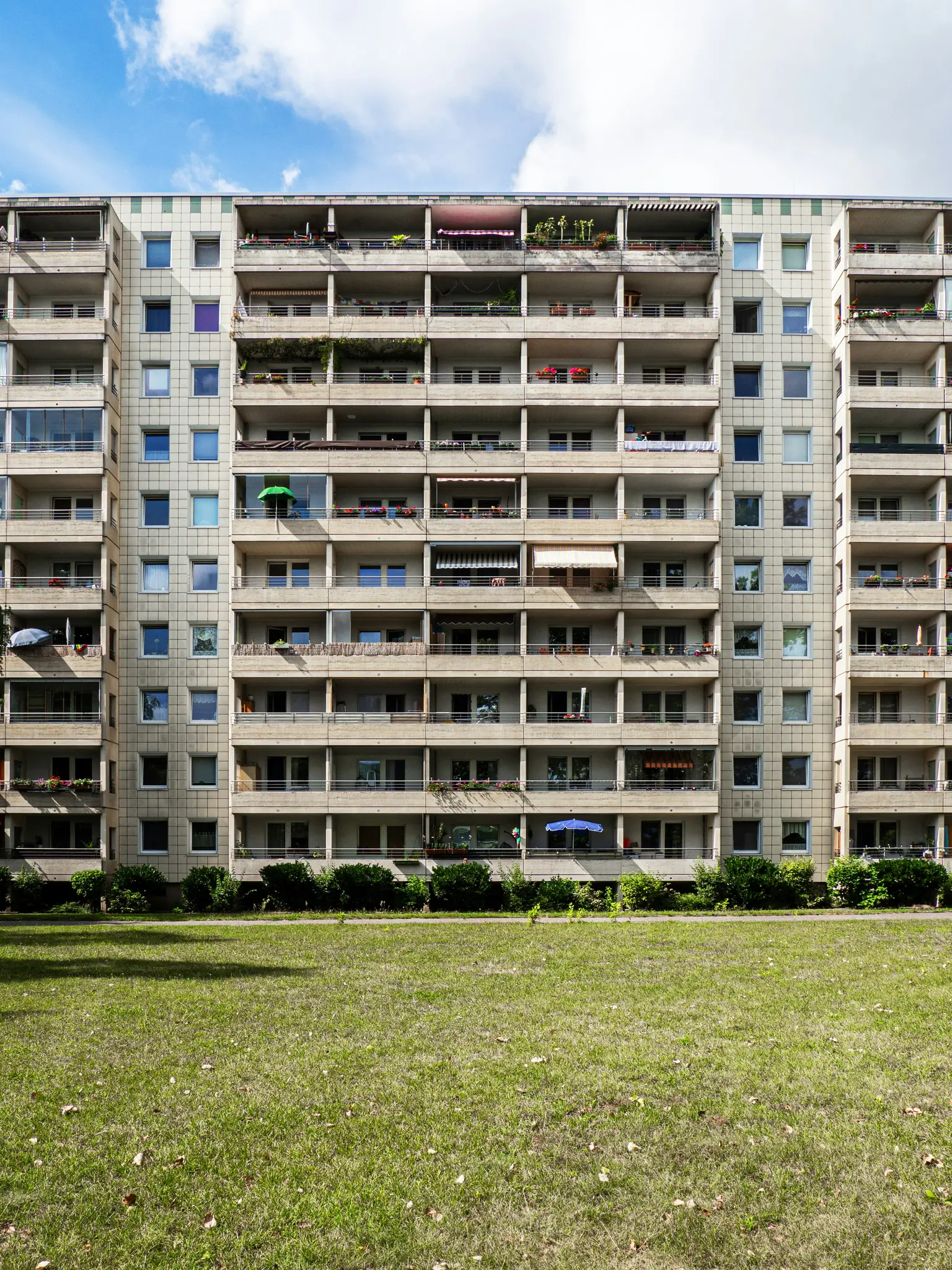 Un edificio de apartamentos alto de varias plantas con numerosos balcones y ventanas, visto desde un amplio césped verde bajo