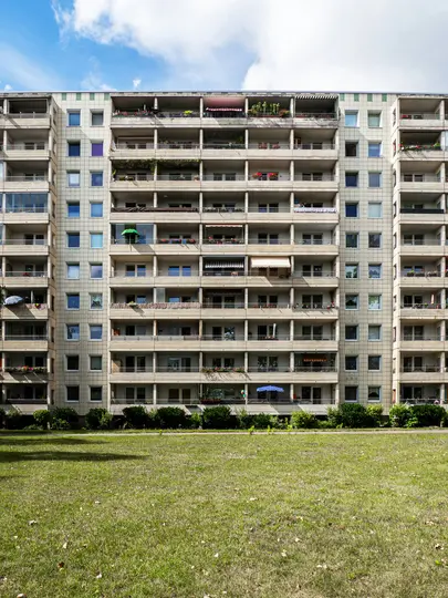 Een hoog, meerlagig appartementengebouw met talrijke balkons en ramen, gezien vanaf een breed groen gazon onder een deels...