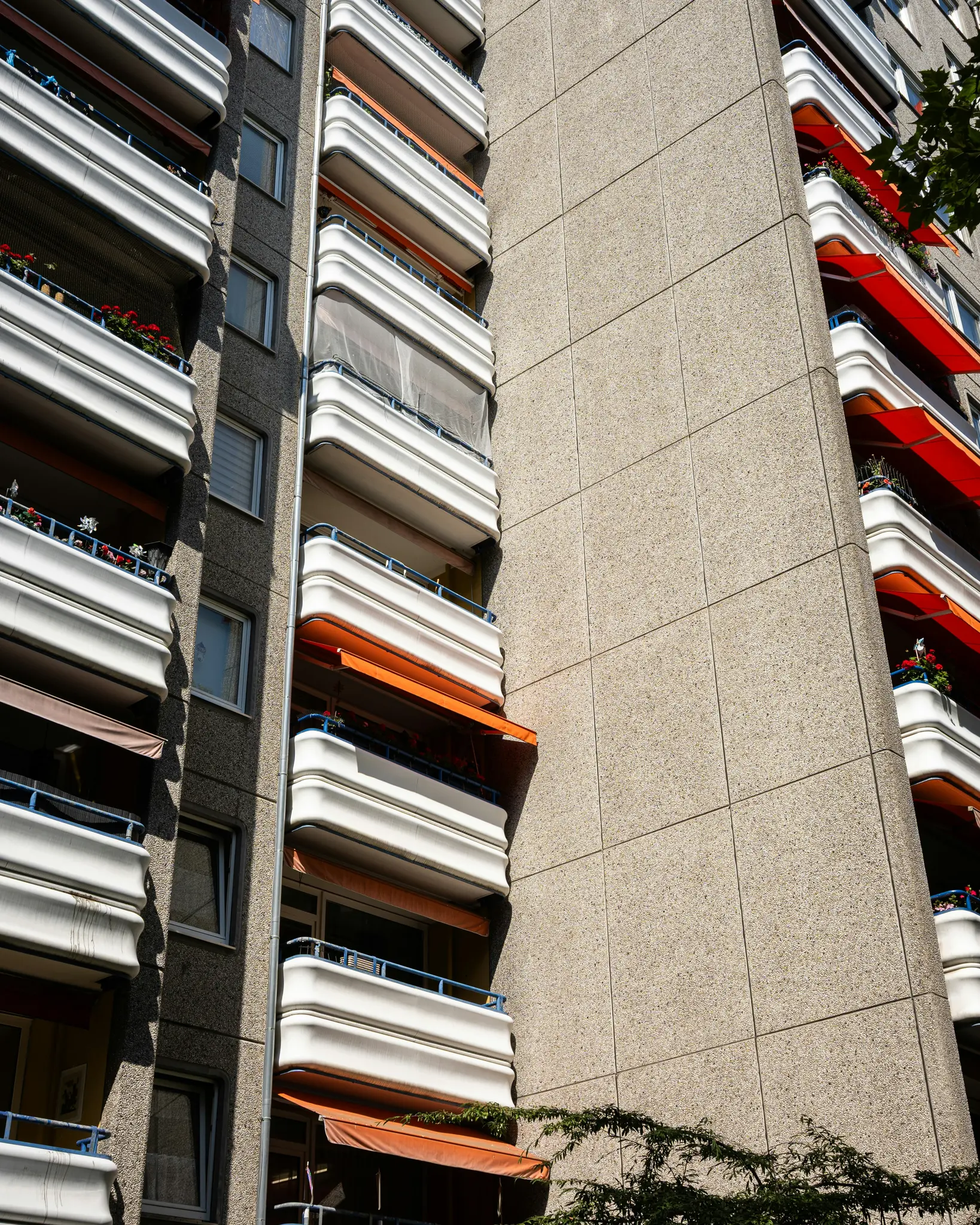 Záber z nízkeho uhla na vysoký obytný dom so sivými stenami, bielymi zakrivenými balkónmi a oranžovými výsuvnými markízami.