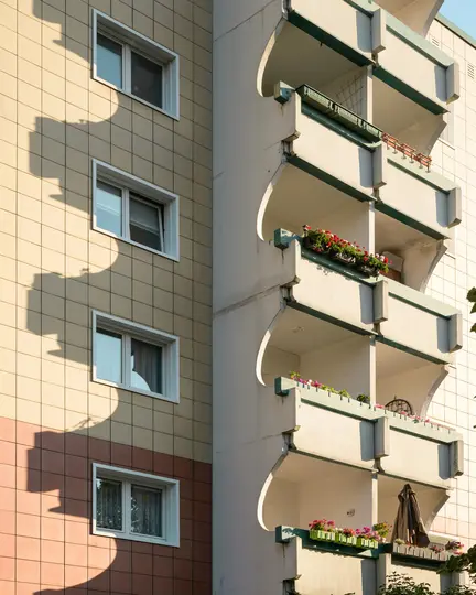 Detailný, slnečný pohľad na fasádu budovy. Ľavá strana má béžové a hnedé obložené steny s bielymi rámami okien. …
