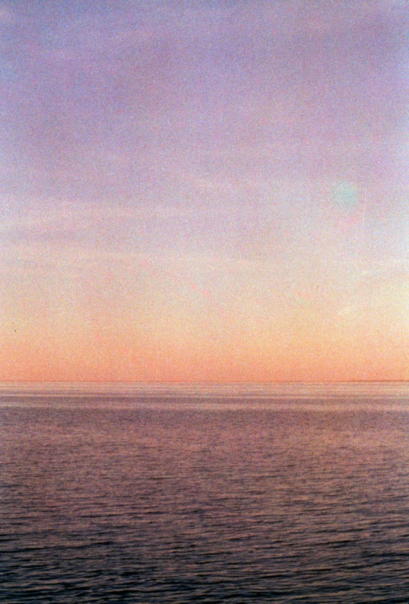 Een minimalistische foto van een zonsondergang of zonsopgang boven de oceaan. De lucht gaat van paars bovenaan naar oranje