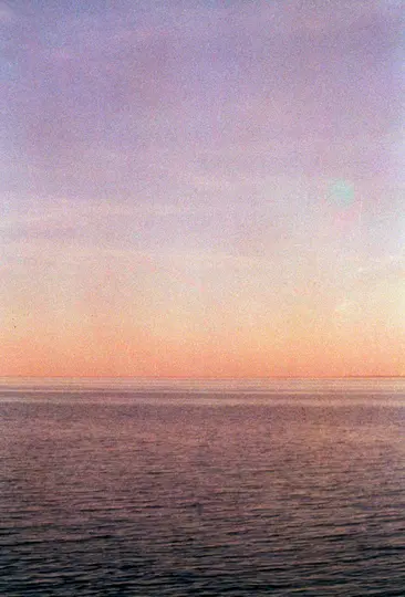 Minimalistická fotografie západu nebo východu slunce nad oceánem. Obloha přechází shora do fialové a dole do oranžové.