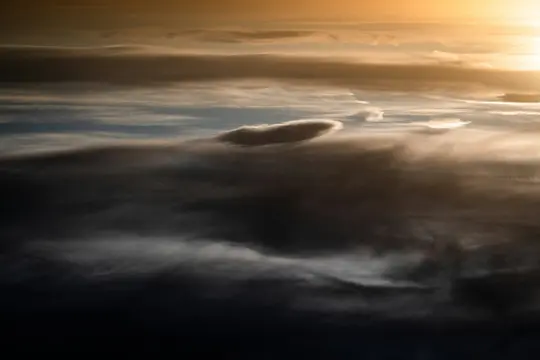 En dramatisk himmel ved gyldne time, med lag af mørkegrå og blå skyer oplyst af et klart orange-gult lys.