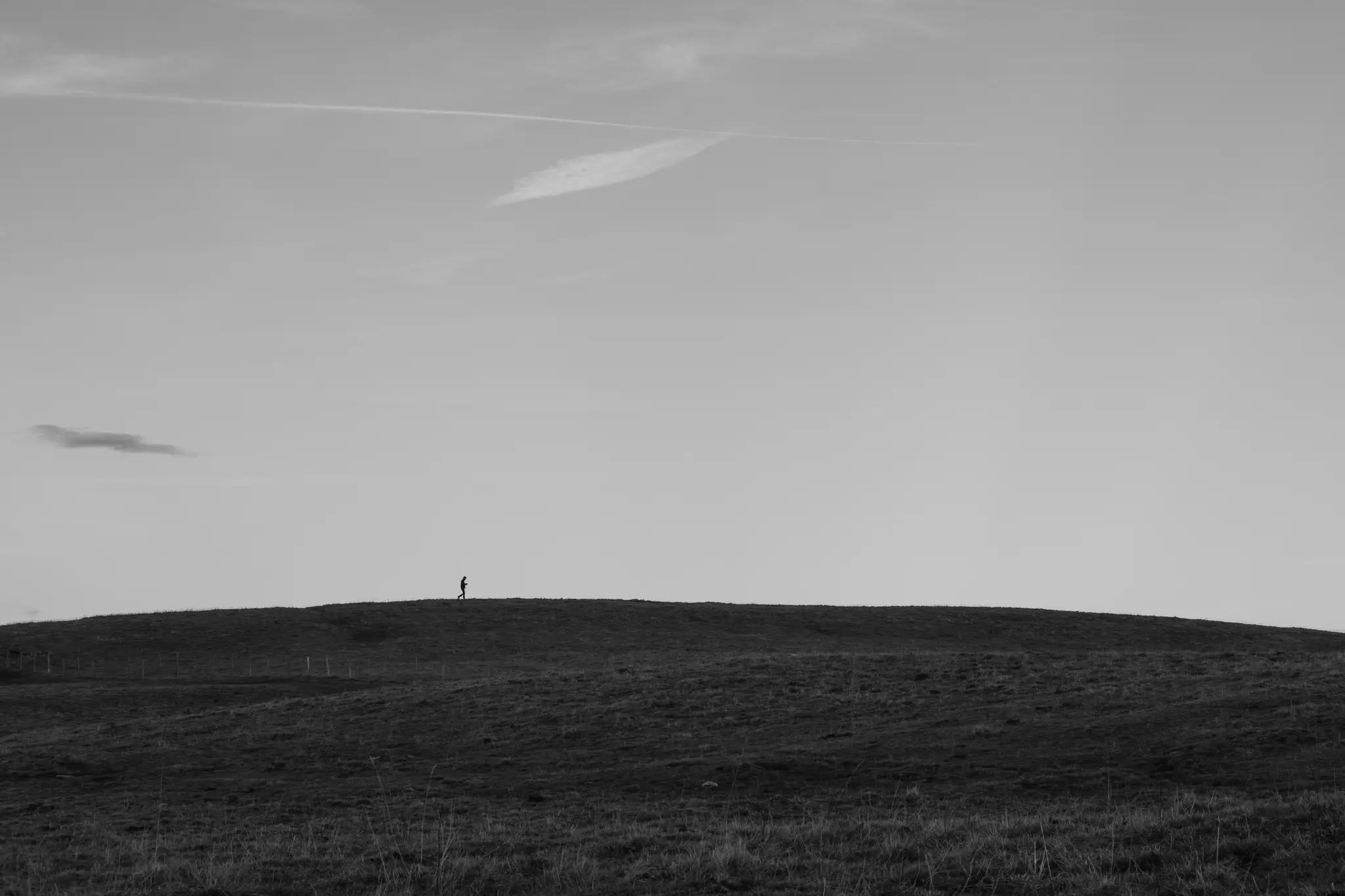 Una foto di paesaggio in bianco e nero mostra una minuscola figura in silhouette che cammina lungo la cresta di una collina