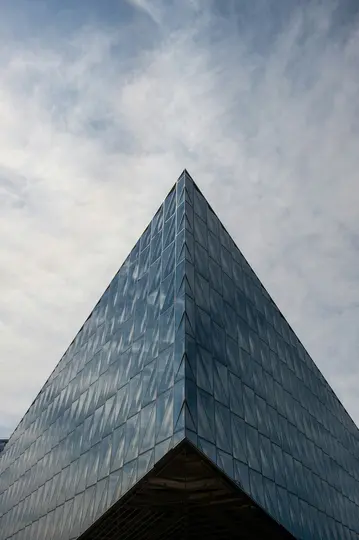 Et lavvinklet billede af en moderne bygning med en pyramideformet glasfacade, der afspejler den skyede himmel.