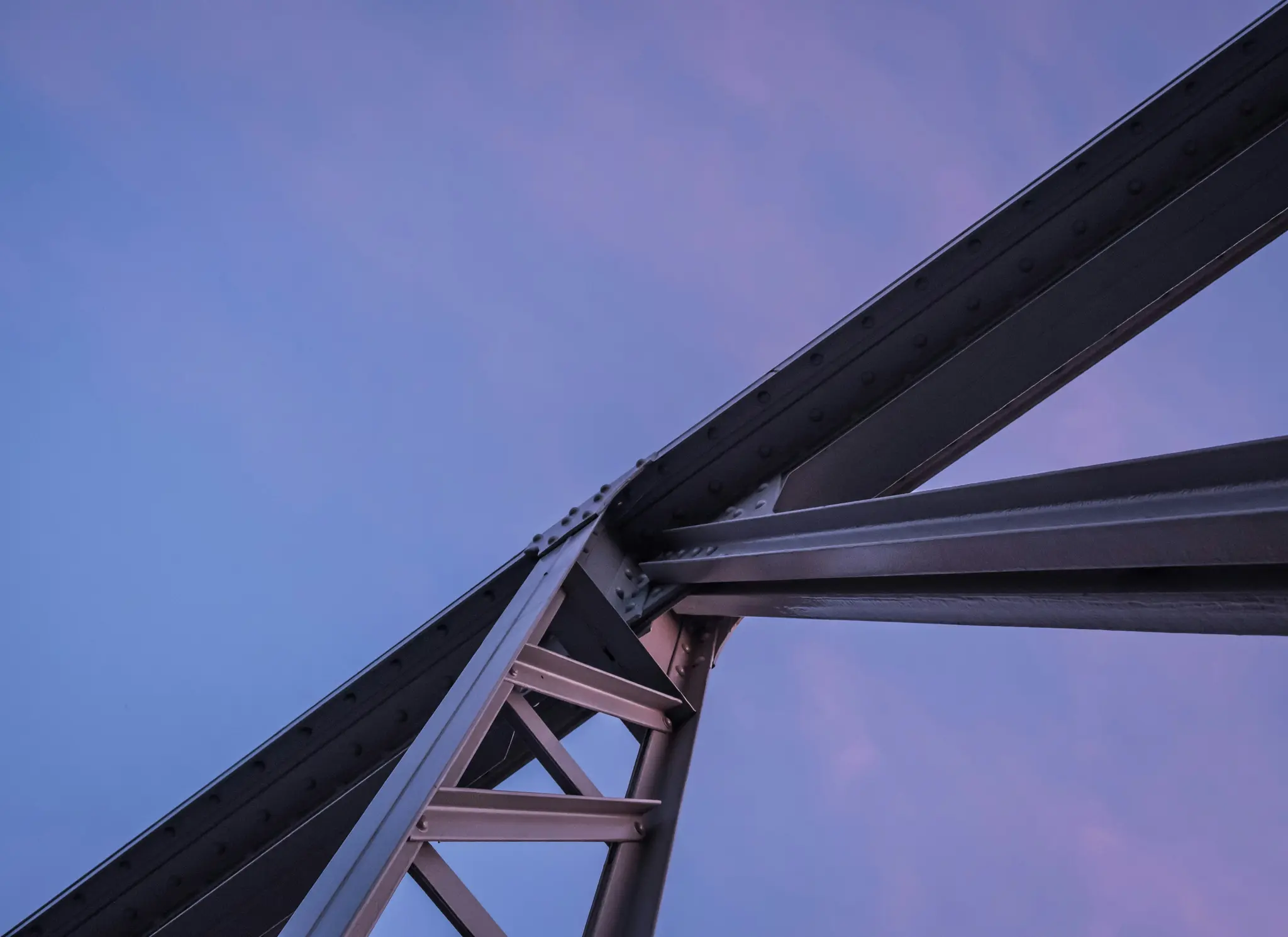 Et lavvinklet billede af et gråt stålbrofag mod en gradient tusmørkehimmel i blå og lilla.
