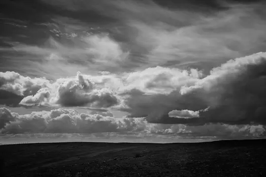 Et sort-hvidt landskabsbillede af et mørkt, tekstureret mark under en himmel fyldt med forskellige typer skyer, fra tynde
