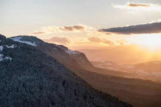 Et betagende bredt landskabsfoto af snedækkede bjerge og dale badet i den varme glød fra en solnedgang.