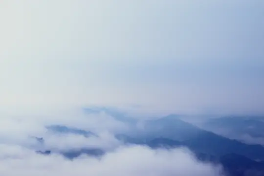 Un'ampia foto paesaggistica che mostra diverse cime montuose parzialmente coperte da un denso strato di nebbia o nuvole