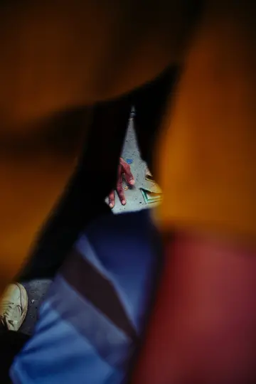 Una mano si protende verso denaro a terra, vista attraverso uno stretto passaggio buio creato da un tessuto sfocato.
