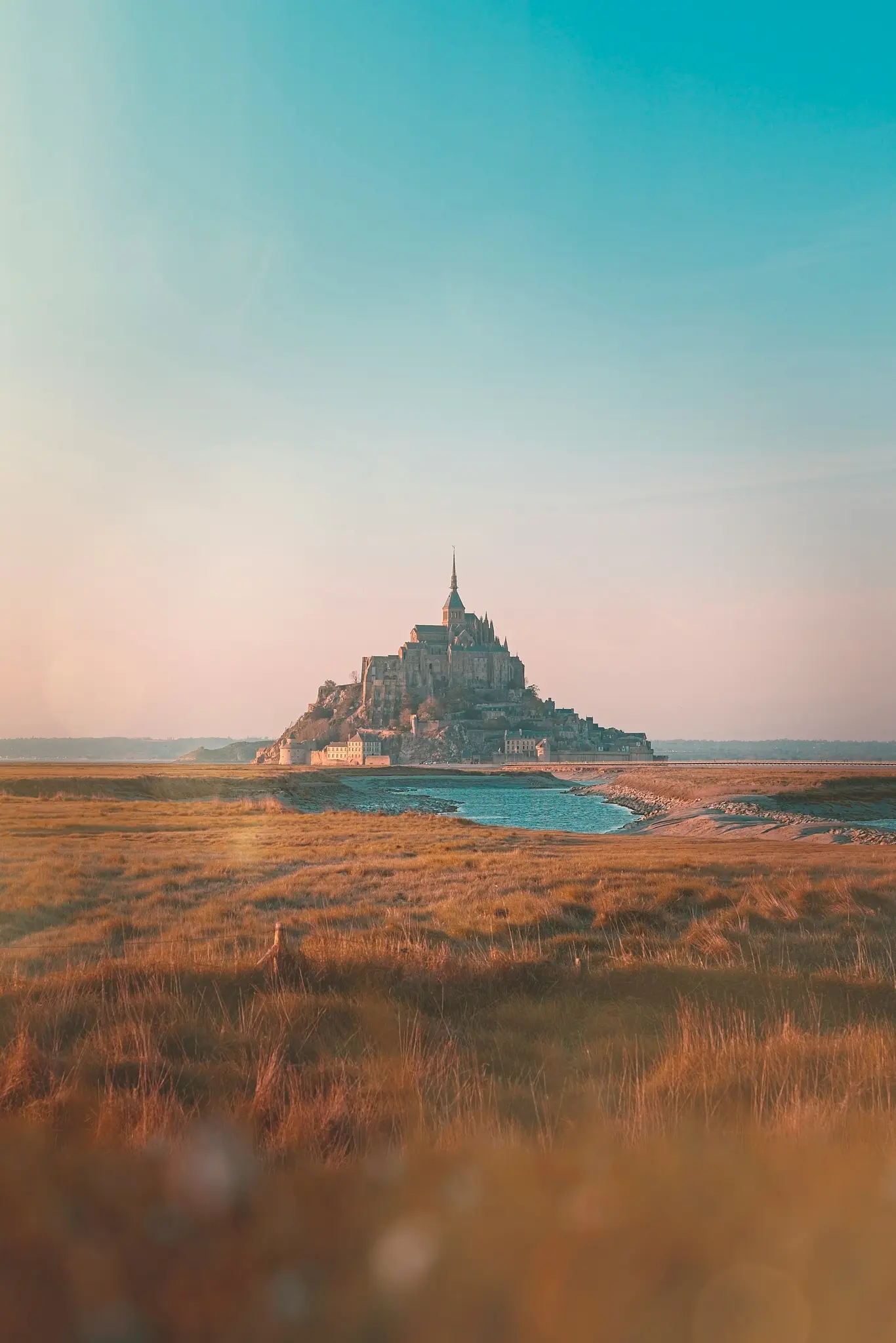 Mont Saint-Michel széles tájképe, egy középkori apátság egy sziklás szigeten, arany óra égbolt alatt.