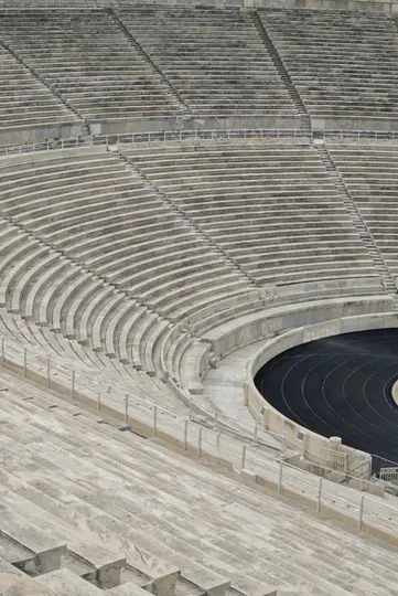 En set fra oven af et tomt stadion, der viser rækker af grå betonpladser, der buer rundt om en sort løbebane.