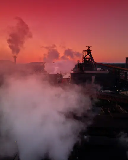 Ein Industriekomplex bei Sonnenuntergang mit einem lebhaften roten und orangen Himmel. Hohe Strukturen stoßen große