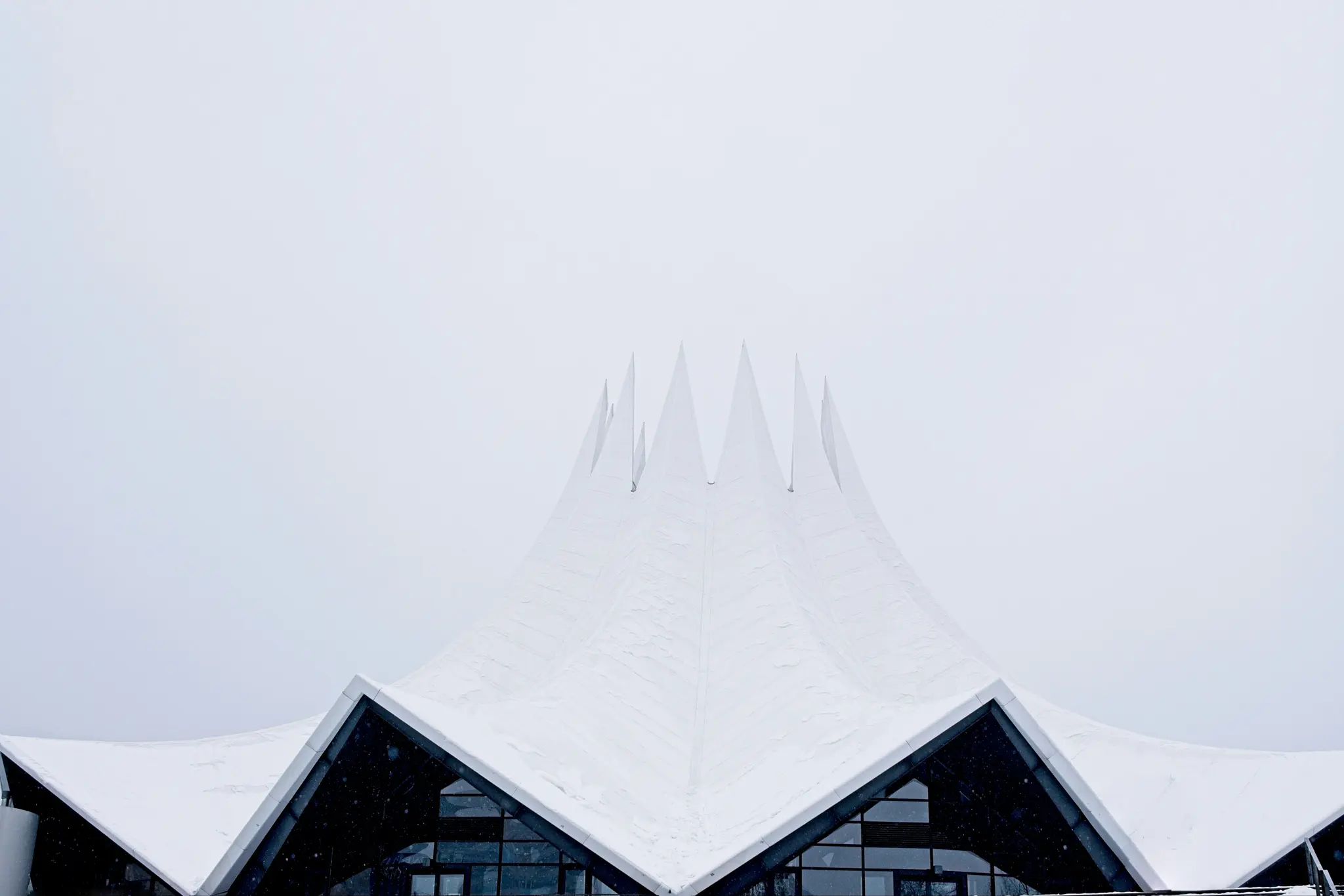 Ein eindrucksvolles Architekturfoto eines modernen, weißen, spitzen Dachs, bedeckt mit Schnee, unter einem hellgrauen Himmel.