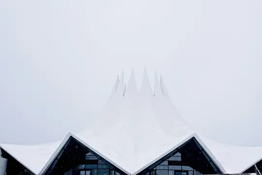 Ein eindrucksvolles Architekturfoto eines modernen, weißen, spitzen Dachs, bedeckt mit Schnee, unter einem hellgrauen Himmel.