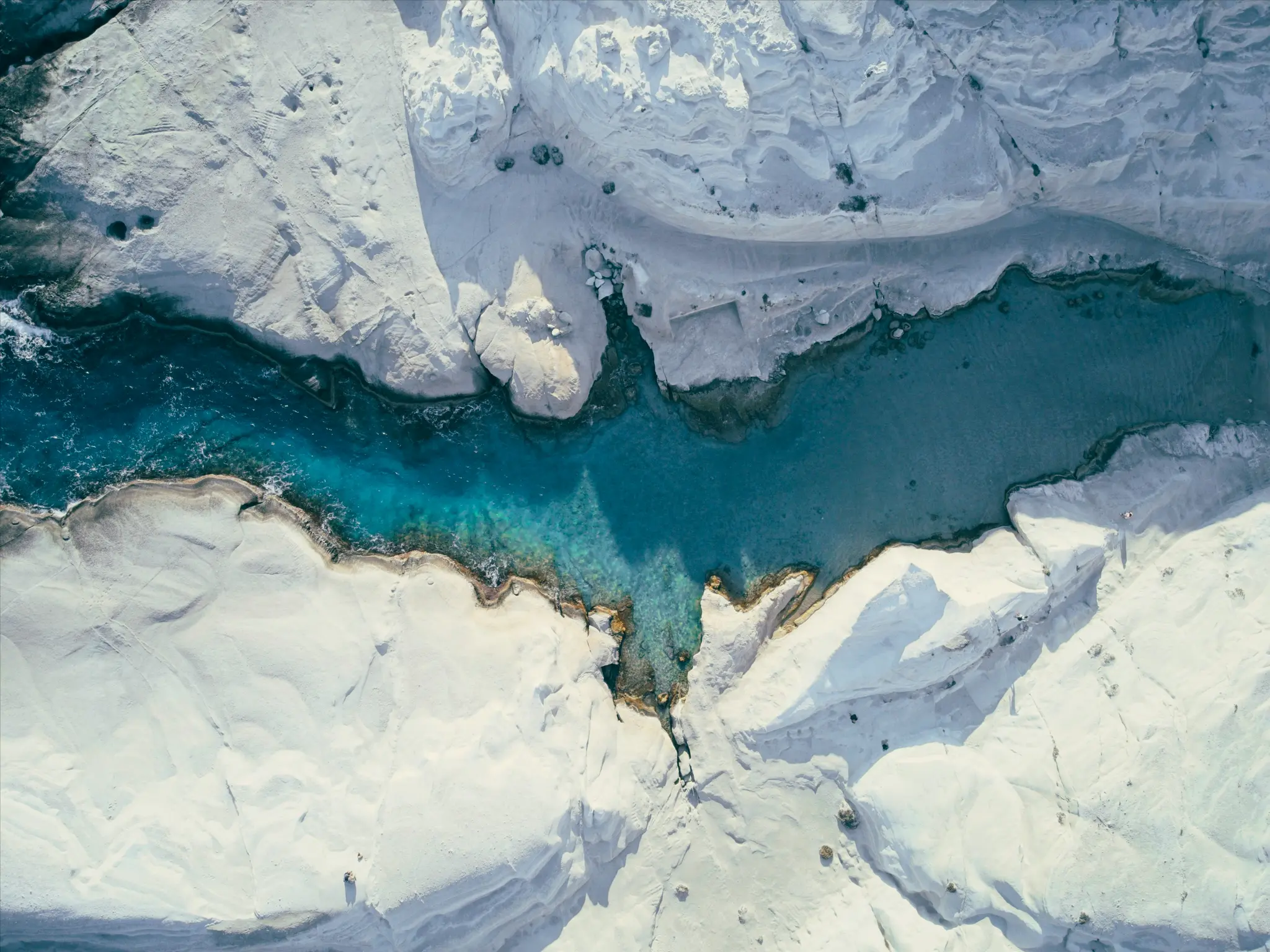 An aerial shot shows a vibrant blue river or inlet snaking through stark white rock formations, with clear water revealing…