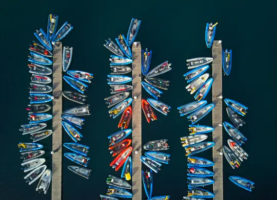 Eine von oben aufgenommene Luftaufnahme eines Yachthafens zeigt viele Schlauchboote, meist blau und grau, die entlang von