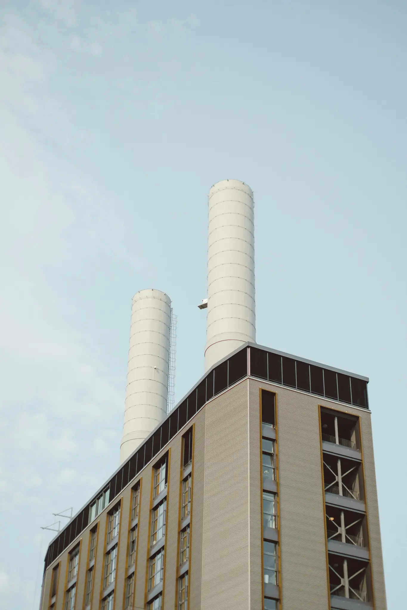 A low-angle view of a modern building featuring a corrugated grey facade and two tall, white industrial chimneys.