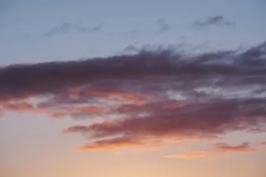 A wide shot of a sky at sunset, featuring a band of dark purple clouds above lighter pink and orange clouds.