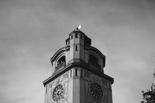 A black and white, low-angle shot of an ornate clock tower with two visible clock faces and decorative carvings.