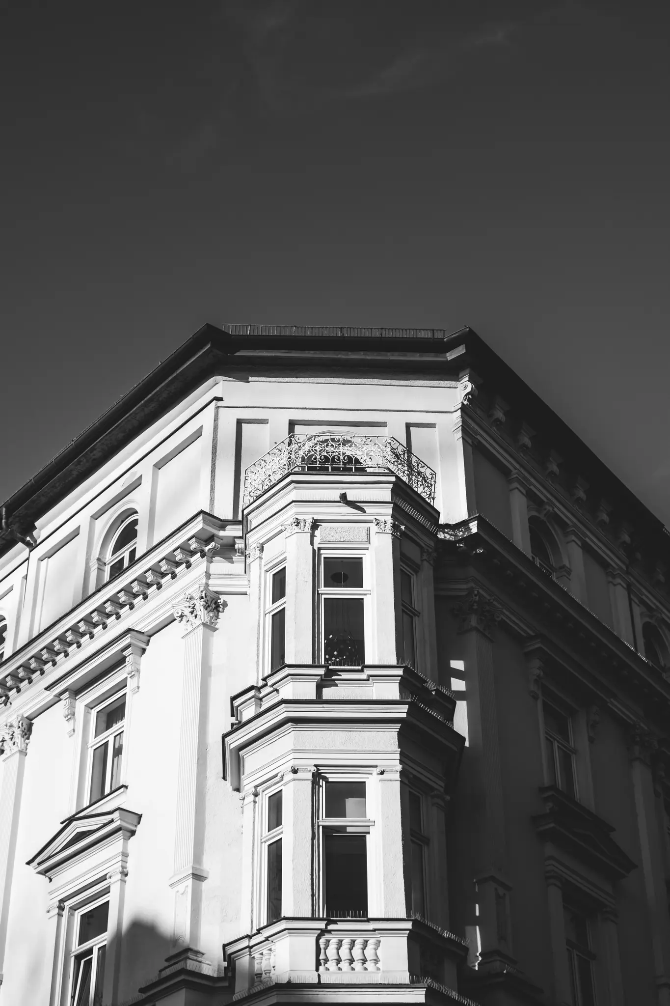 En svartvit bild av ett gammalt byggnadshörn med burspråk, en liten balkong och dekorativ arkitektur…