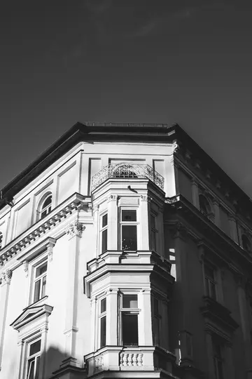 Et sort-hvidt billede af en gammel bygnings hjørne med karnapper, en lille altan og dekorativ arkitektur…