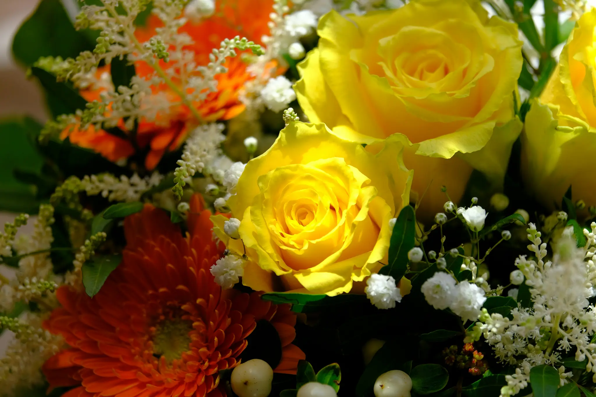 Nærbillede af en buket med klare gule roser, en orange gerbera, hvid gypsophila og grønt løv.